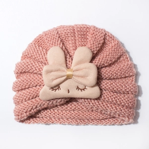 Close-up of pink knitted baby hat with cute beige rabbit doll and a large bow decor