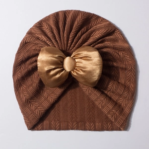 Détail d'un bonnet turban en maille marron avec un grand nœud en satin doré