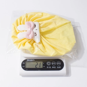 Dettaglio del cappello da neonato a coniglio giallo che pesa 21g su una bilancia