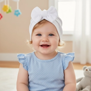 Detailed view of white waffle knit baby hat with a large decorative bow on infant model