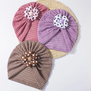 Three newborn beanies with polka dot flowers on a rustic woven mat for a cozy style