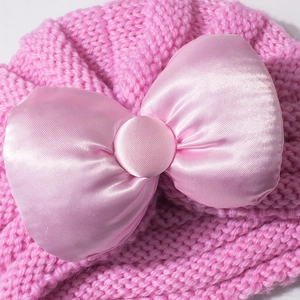 Vue détaillée d'un bonnet en maille rose pour bébé avec un grand nœud élégant en satin