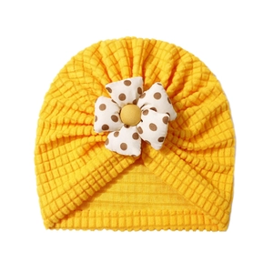 Detail of yellow baby turban hat with waffle texture and a large polka dot fabric flower