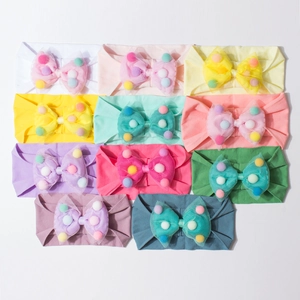 Flat lay of 11 colorful baby headbands with mesh bows and soft pom-poms on white background