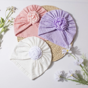Detailed knit texture of baby turban hats with large fabric roses on a woven mat