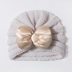 Gros plan du bonnet tricoté pour bébé avec un grand nœud en satin champagne et texture
