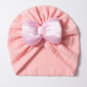 Détail du bonnet turban rose pour bébé avec un grand nœud en satin et texture tricotée