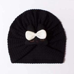Detail of baby turban hat featuring black waffle texture and a large white bow with eyelashes