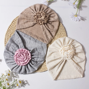 Detail view of knitted baby turban hats with silk rose flowers on a woven mat