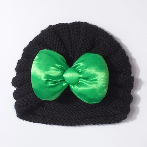 Détail d'un bonnet tricoté pour bébé avec un grand nœud en satin vert émeraude brillant