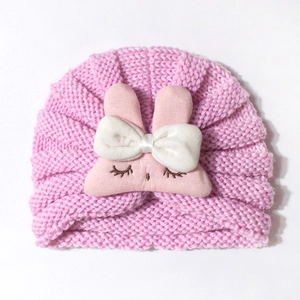 Detailed knit texture of pink baby turban hat featuring plush bunny ears and white bow