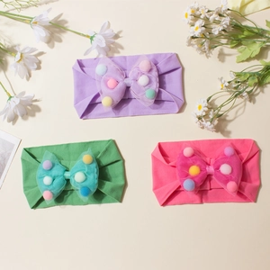 Detailed view of three soft baby headbands with tulle bows and colorful pom-poms