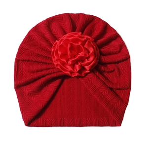 Detail of red knitted baby turban cap featuring a large satin rose and textured pleats