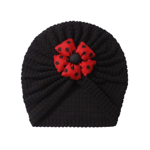Detail of baby turban hat showing black waffle knit fabric and red polka dot flower