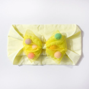 Detailed close-up of yellow baby headband with colorful pom-poms inside mesh bow