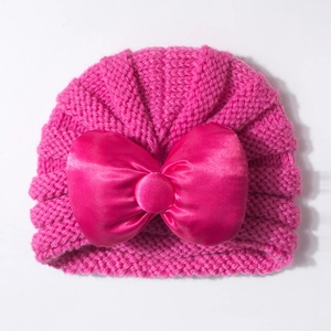 Détail d'un bonnet tricoté pour bébé avec un grand nœud en satin rose et texture côtelée