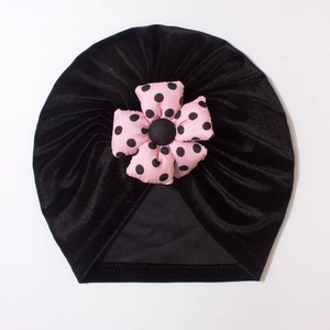 Detailed view of black velvet baby turban hat with a pink polka dot flower ornament