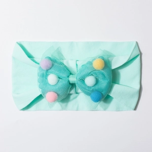 Detailed close-up of mint green baby headband with mesh bow and colorful pom-poms
