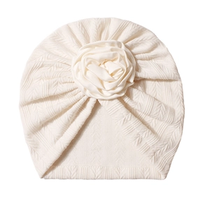 Detailed view of cream baby turban hat featuring a large satin rose and ribbed knit texture