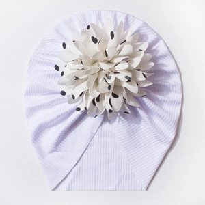 Détail d'un bonnet bébé en maille côtelée blanche avec une grande fleur à pois noirs
