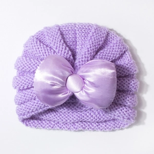Détail du bonnet en tricot violet pour bébé avec un grand nœud en satin sur fond blanc