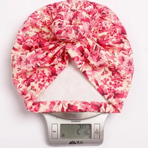 Detail showing the lightweight 27.2g baby turban hat with pink floral print on a scale