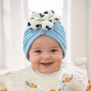 Detail of baby turban hat in light blue with large white flower and black heart print