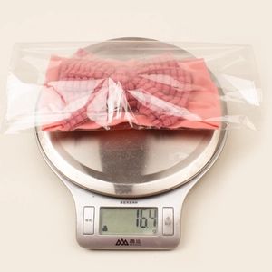 Detailed view of dusty rose ribbed bow headband for babies, weighed on scale for size check