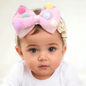 Close-up of pink mesh bow headband with colorful pom-poms on floral lace for baby