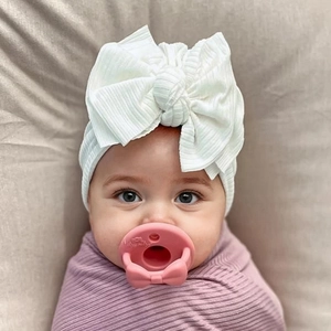 Close-up of baby headwrap with large white bow and ribbed knit texture on infant model