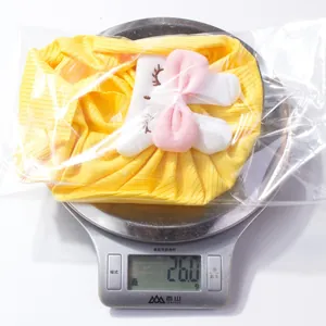 Detail view of a yellow knitted baby hat with bunny ears on a digital scale weighing 26g