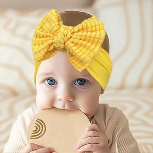 Close-up of baby girl wearing a vibrant yellow waffle knit bow headband with soft nylon band