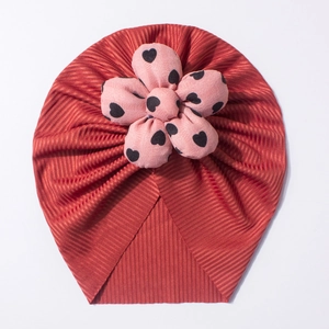 Detail shot of the brick red ribbed baby turban hat with a pink polka dot fabric flower