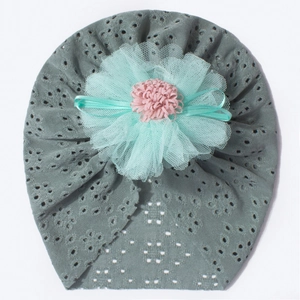 Detail of baby fontanelle hat featuring mint green mesh petals and pink pompom on grey lace
