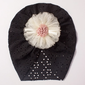 Detail of baby lace turban hat featuring a black mesh fabric and a large handmade flower