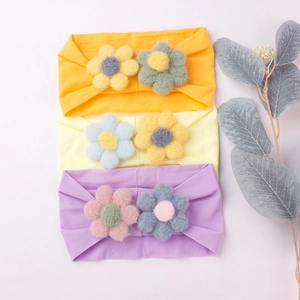 Detailed view of three elastic nylon baby headbands with handmade plush flowers in soft colors