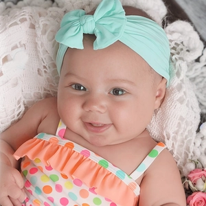 Infant mint green bow headband with colorful polka dot ruffled swimsuit on lace background