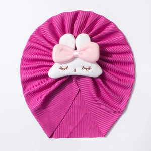 Detail of baby bunny turban hat in purple ribbed fabric with plush rabbit doll and bow