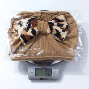 Brown striped infant headband with a large leopard print bow being weighed on a scale