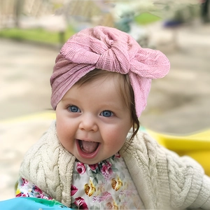 Pink ribbed baby turban hat with large bow detail worn by a smiling infant girl