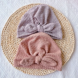 Knitted infant turban hats with large bows in pink and purple colors on a straw mat