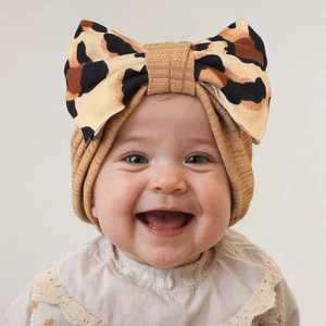 Close-up of baby girl wearing camel ribbed knit hat with oversized leopard print bow