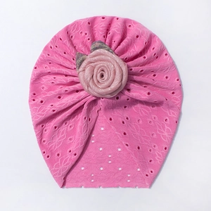 Dettaglio del cappello da neonato rosa con pizzo floreale traforato e grande rosa in tessuto 3D