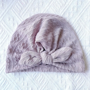 Detailed texture of baby knitted beanie with large bow decoration on ribbed fabric