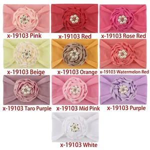 Flat lay of baby nylon headbands with satin flowers and pearl rhinestone centers in 10 colors