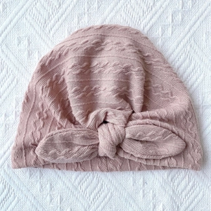Close-up of pink cable knit baby hat featuring a soft rabbit ear bow decoration