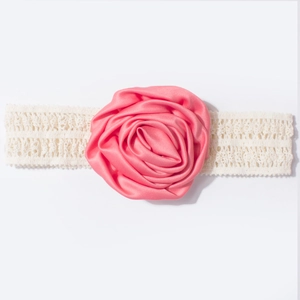 Détail d'une rose en soie rose sur un bandeau de bébé en dentelle crème à texture fine