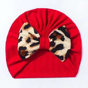 Close-up of baby beanie featuring red ribbed knit fabric and a leopard print bow