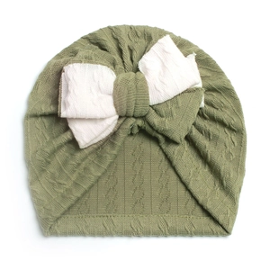 Detail of soft green knit baby turban hat featuring a large off-white bow and ribbed texture