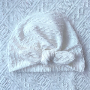 Detailed view of white cable knit baby turban hat with a large soft knot bow decoration